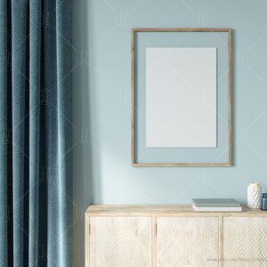 May include: A light blue wall with a wooden frame holding a blank white poster. A wooden cabinet with white geometric designs sits below the poster. A teal blue curtain is on the left side of the image.