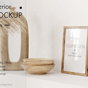 Könnte beinhalten: Ein Holzrahmen-Mockup mit weißem Hintergrund. Der Rahmen ist 8x12 Zoll oder 21 cm x 30 cm groß. Der Text "YOUR DESIGN" ist auf dem weißen Passepartout im Rahmen gedruckt. Der Rahmen steht auf einem weißen Regal mit einer Holzschale im Hintergrund.