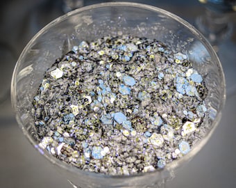 May include: A glass bowl filled with silver, black, and blue glitter. The glitter is a mix of different sizes and shapes.