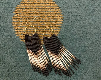 May include: A pair of long, beaded earrings with a brown and beige ombre design. The earrings are made with small, round beads and have a gold-toned wire.