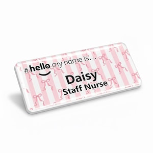 Può includere: Un badge nominativo rettangolare con sfondo a righe rosa e bianche e dettagli di fiocchi rosa. Il badge riporta la scritta "#hello my name is..." sopra il nome "Daisy" e il titolo "Staff Nurse".