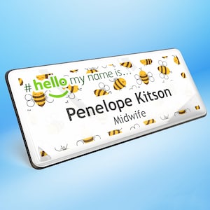 Puede incluir: Una placa de identificación rectangular con fondo blanco y borde negro. La placa presenta el texto "#hello my name is..." y "Penelope Kitson, Midwife." El diseño incluye abejas de dibujos animados en amarillo y negro.