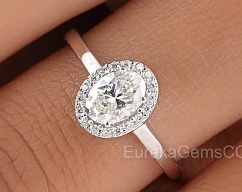 May include: A silver ring with an oval-shaped diamond surrounded by a halo of smaller diamonds.