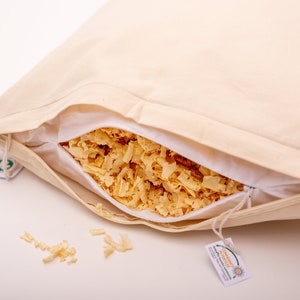 Puede incluir: Una funda de almohada blanca con una cremallera está abierta, revelando un relleno de virutas de madera. La funda de almohada tiene una etiqueta verde y blanca adjunta.