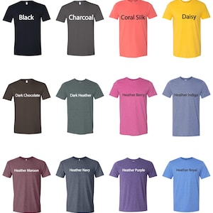 Op de afbeelding: Assortiment effen t-shirts in diverse kleuren, waaronder zwart, houtskool, koraalzijd en madeliefjesgeel. Andere kleuren zijn donkere chocolade, donker heather, heather berry, heather indigo, heather maroon, heather navy, heather purple en heather royal. Elk shirt heeft een label met de kleurnaam.