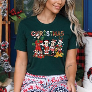 Puede incluir: Camiseta verde oscuro con la palabra "CHRISTMAS" en un dise&ntilde;o festivo y colorido. La camiseta muestra personajes de dibujos animados con atuendos navide&ntilde;os, incluyendo Mickey y Minnie Mouse, y Chip y Chop. Una camiseta alegre con tem&aacute;tica navide&ntilde;a.