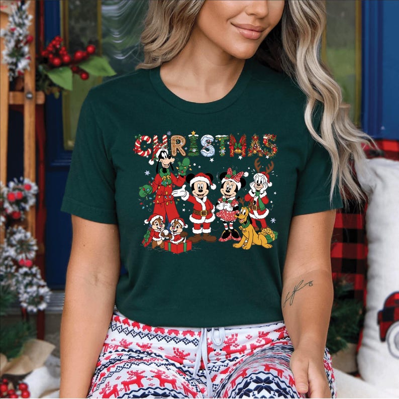 Puede incluir: Camiseta verde oscuro con la palabra "CHRISTMAS" en un dise&ntilde;o festivo y colorido. La camiseta muestra personajes de dibujos animados con atuendos navide&ntilde;os, incluyendo Mickey y Minnie Mouse, y Chip y Chop. Una camiseta alegre con tem&aacute;tica navide&ntilde;a.