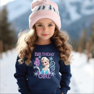 Puede incluir: Una ni&ntilde;a lleva una sudadera azul marino y un gorro rosa, con un fondo de escena invernal. La sudadera presenta el texto "BIRTHDAY 4 GIRL" con una imagen de princesa y copos de nieve.