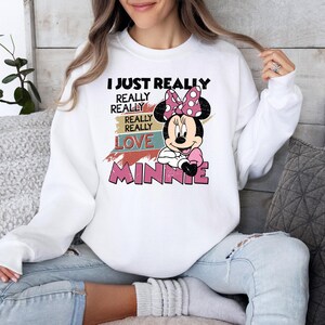 May include: White sweatshirt featuring a graphic of Minnie Mouse with a pink bow and the text "I JUST REALLY REALLY REALLY LOVE MINNIE" in black and pink. The sweatshirt is a casual style.