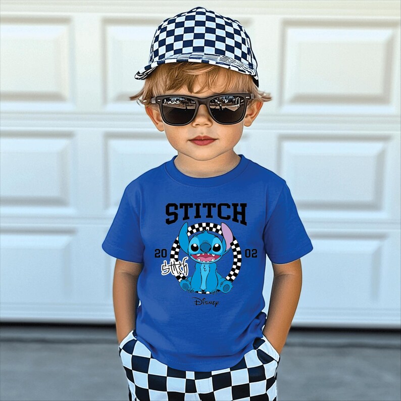 Puede incluir: Un ni&ntilde;o peque&ntilde;o con una camiseta azul con un gr&aacute;fico de Stitch, una gorra de b&eacute;isbol a cuadros y gafas de sol. La camiseta lleva la palabra "STITCH" encima del personaje y el logotipo de Disney debajo. El ni&ntilde;o tambi&eacute;n lleva pantalones cortos a cuadros.