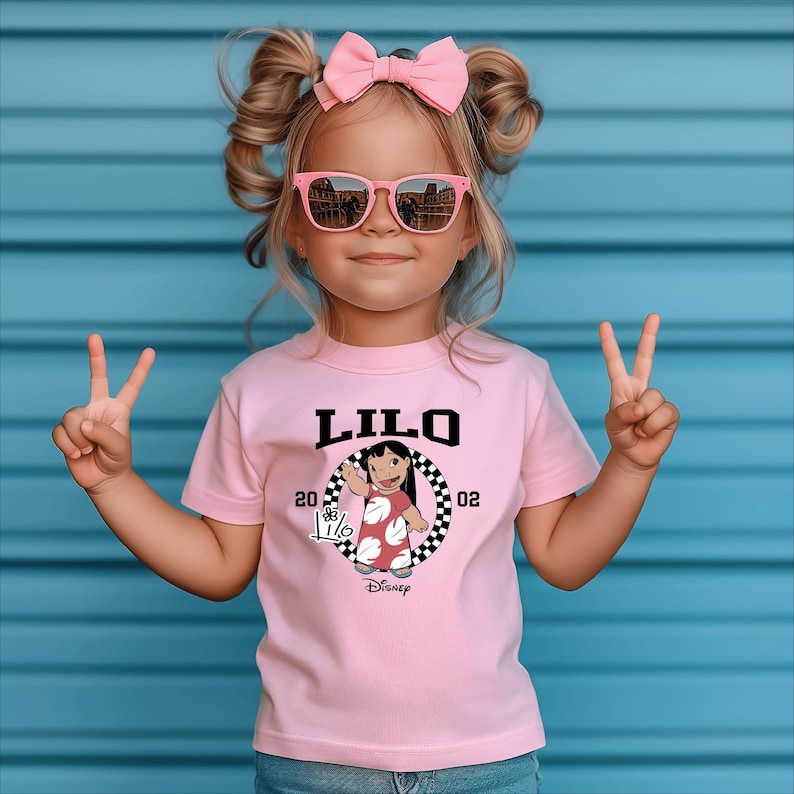 Puede incluir: Una ni&ntilde;a lleva una camiseta rosa con la palabra "LILO" en letras negras. La camiseta presenta un dibujo de un personaje de dibujos animados y el logotipo de Disney. La ni&ntilde;a tambi&eacute;n lleva gafas de sol rosas y un lazo rosa.