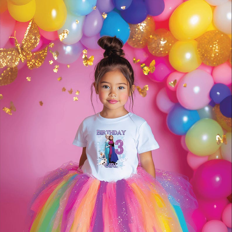 May include: A young girl wearing a white t-shirt with a graphic of two characters and the number 3, with the word "BIRTHDAY" above and "GIRL" below. She is wearing a colorful rainbow tutu skirt. The background includes balloons and butterflies.