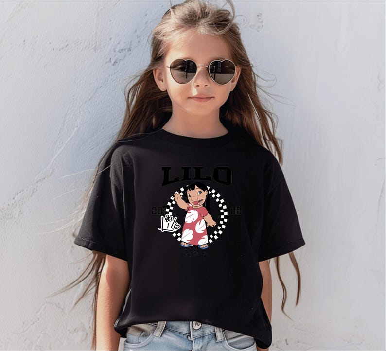 Puede incluir: Camiseta negra con la palabra "LILO" encima de una imagen de dibujos animados de una ni&ntilde;a con un vestido rojo con lunares blancos. La imagen est&aacute; rodeada por un c&iacute;rculo a cuadros blanco y negro. La camiseta tambi&eacute;n tiene el texto "2002" y un signo de mano.