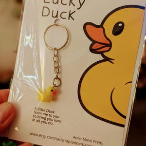 May include: A yellow rubber duck keychain with a silver chain and ring. The keychain is packaged on a white card with the text "Lucky Duck" and "A little Duck from me to you to bring you luck in all you do". The card also includes the website address "www.etsy.com/uk/shop/annemariepretty" and the name "Anne-Marie Pretty".