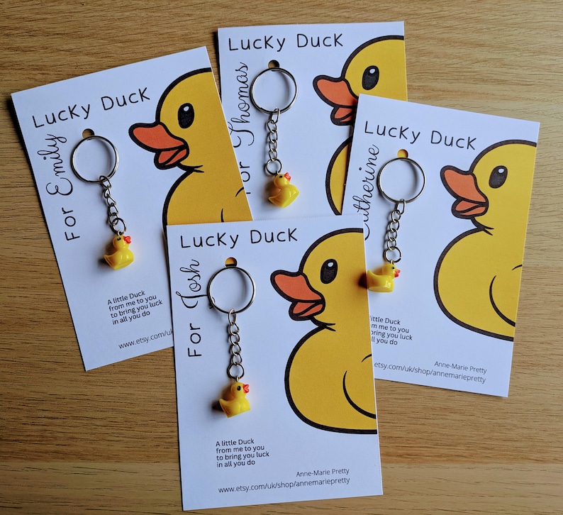 May include: Four white cards with yellow rubber duck keychains attached. Each card has the text "Lucky Duck" and a name, "For Emily", "For Thomas", "For Josh", and "Catherine". The cards have a message about the duck bringing good luck.
