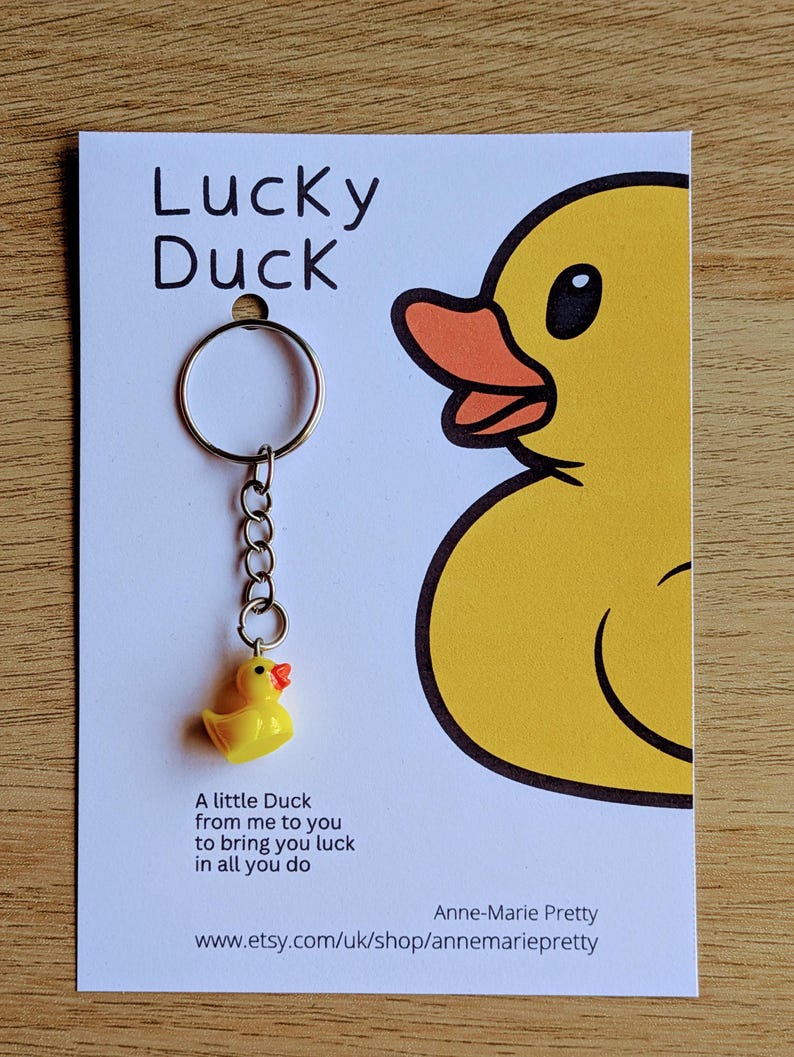 May include: A yellow rubber duck keychain with a silver chain and a ring. The duck has a red beak and orange feet. The keychain comes with a card that says "Lucky Duck" and "A little Duck from me to you to bring you luck in all you do." The card also includes the name "Anne-Marie Pretty" and the website "www.etsy.com/uk/shop/annemariepretty".