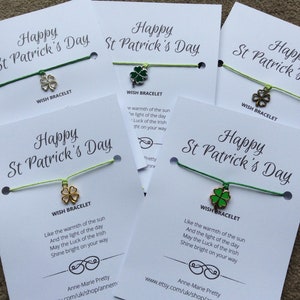Könnte beinhalten: Drei weiße Karten mit grünen und goldenen Schnurarmbändern. Jede Karte trägt den Text "Happy St. Patrick's Day" und ein Glücksarmband mit einem Kleeblatt-Anhänger. Der Text auf den Karten lautet: "Wie die Wärme der Sonne und das Licht des Tages. Möge das Glück der Iren auf deinem Weg leuchten."