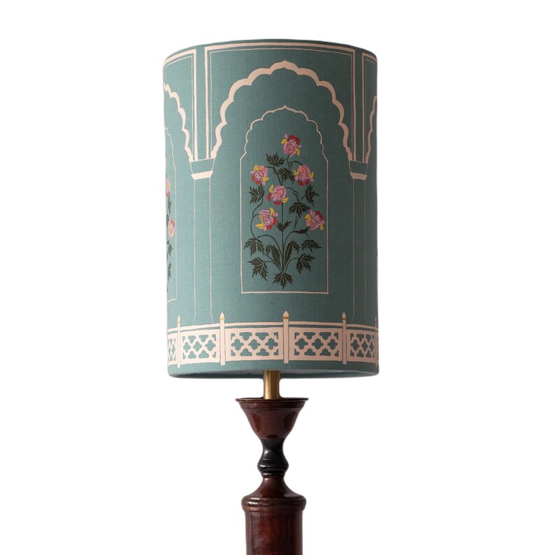 May include: A teal blue lampshade with a white floral design and a white lattice border. The lampshade is on a brown wooden lamp base.