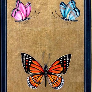 May include: A framed painting of three butterflies. The butterflies are painted in a realistic style with vibrant colors. The top two butterflies are smaller and have a more delicate appearance. The bottom butterfly is larger and has a more bold appearance. The butterflies are all set against a gold background.