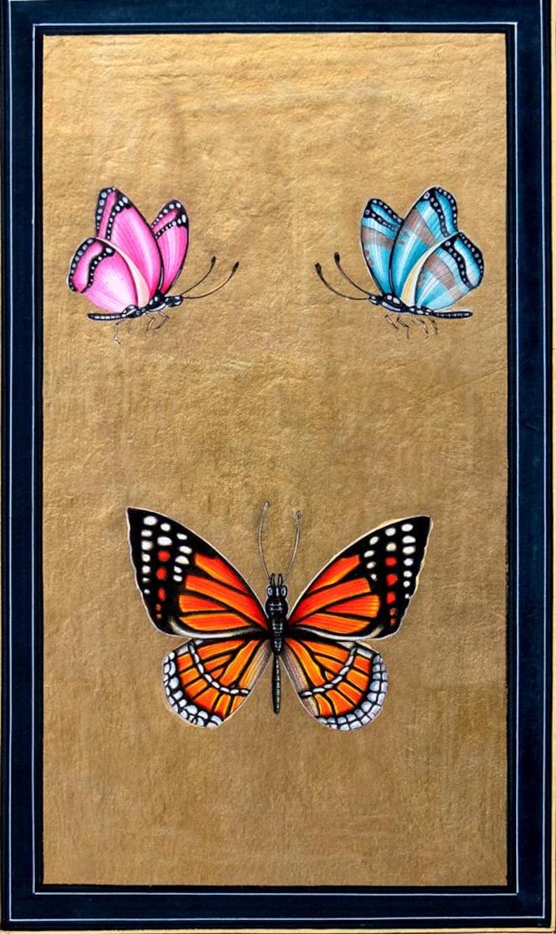 May include: A framed painting of three butterflies. The butterflies are painted in a realistic style with vibrant colors. The top two butterflies are smaller and have a more delicate appearance. The bottom butterfly is larger and has a more bold appearance. The butterflies are all set against a gold background.
