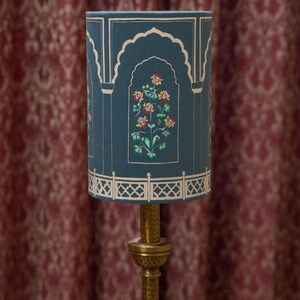 May include: A teal blue lampshade with a white floral design and gold accents. The lampshade has a decorative border with a repeating pattern.