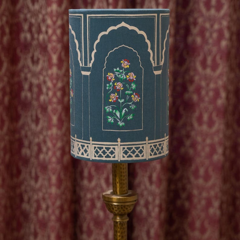 May include: A teal blue lampshade with a white floral design and gold accents. The lampshade has a decorative border with a repeating pattern.