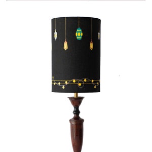 May include: Black lampshade with a gold string of lights and hanging lanterns in shades of green, yellow, and white.