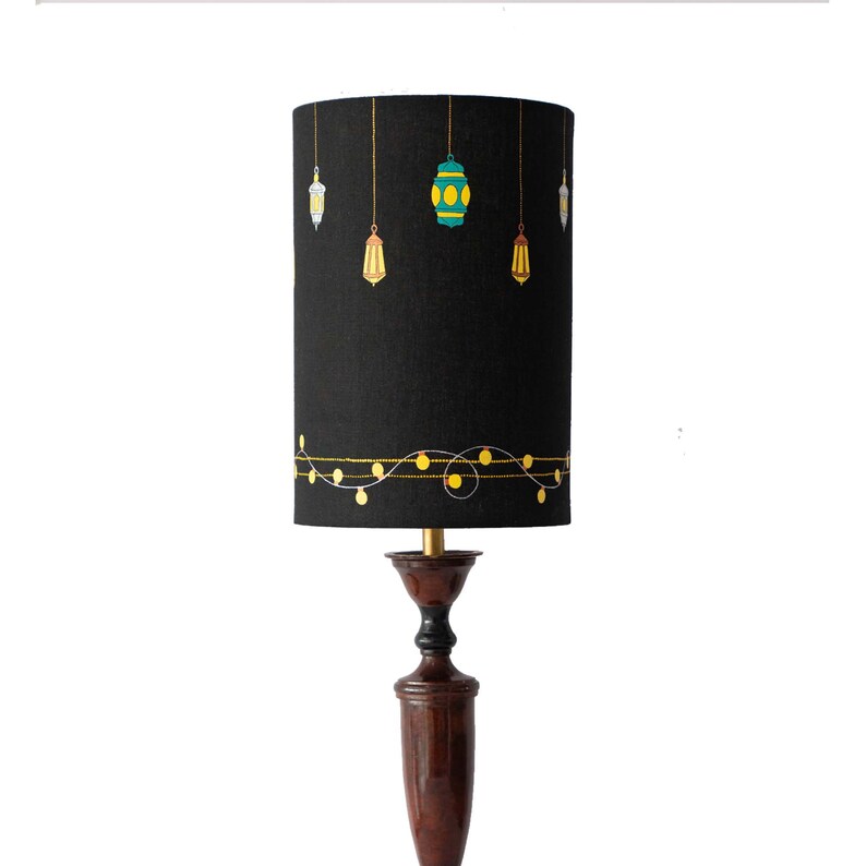 May include: Black lampshade with a gold string of lights and hanging lanterns in shades of green, yellow, and white.