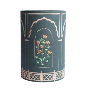 May include: A teal blue lampshade with a floral design. The design features a white archway with a pink and yellow flower motif. The bottom of the lampshade has a white and gold patterned border.