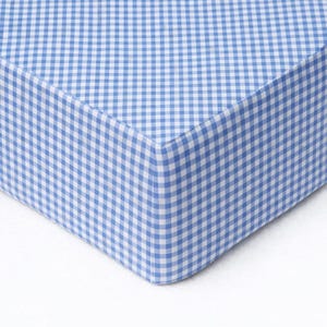May include: Close-up of a blue and white gingham fabric. The fabric is a classic pattern of small, evenly spaced squares. The corner of the fabric is visible, showing the material's thickness and the neat stitching.