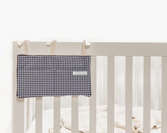 Peut inclure: Un lit de bébé avec un tour de lit à motif pied-de-poule bleu marine et blanc. Le tour de lit est fixé au lit avec des rubans crème. Le lit est peint en gris clair et la literie est blanche. Le label lit "LITTLE MAX".