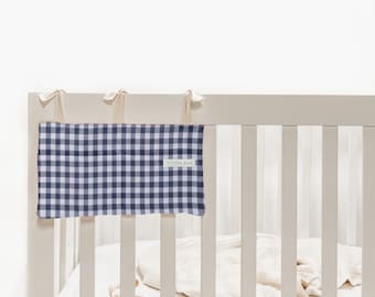 Peut inclure: Un protège-barrière de lit à carreaux vichy bleu marine et blanc, avec le texte "LITTLE MAN" sur une étiquette blanche. Le protège-barrière est attaché au lit avec des rubans crème. Le lit est blanc.