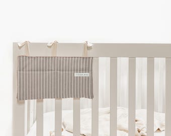 Peut inclure: Un tour de lit à rayures verticales beiges et grises avec une étiquette « LITTLE MAN ». Le tour de lit est attaché à un lit bébé blanc avec des rubans crème. Le lit bébé contient un drap et une couverture blancs.