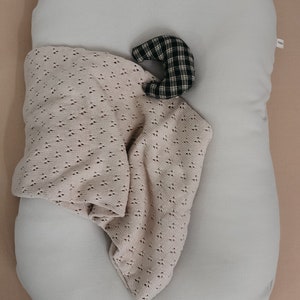 May include: A light gray oval-shaped pillow with a beige crocheted blanket and a black and white plaid crescent-shaped pillow on top.
