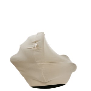 May include: A beige, pleated, stretchy baby carrier cover. The cover is designed to fit over a car seat or stroller and provides privacy and warmth for a baby.