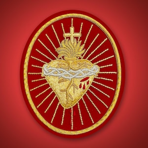 May include: An oval-shaped embroidered patch featuring a gold-colored Sacred Heart design on a red background. The heart is encircled by a silver crown of thorns, topped with a gold cross and flames, and surrounded by radiating gold sunburst rays.