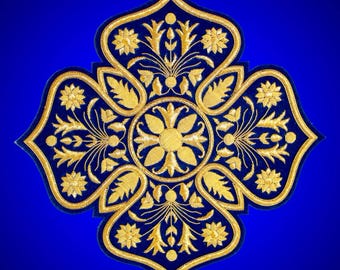 May include: A four-lobed patch featuring intricate gold embroidery on a deep blue fabric base. The design showcases a central floral motif surrounded by symmetrical botanical patterns, including stylized leaves and small blossoms in gold thread.