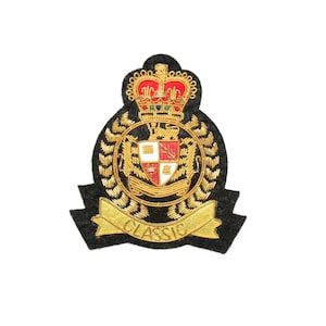 May include: A black embroidered patch with a gold crown, shield, and laurel wreath design. The shield features red and white sections. A gold banner at the bottom reads "CLASSIC".