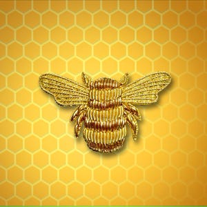 Puede incluir: Una abeja bordada en oro con un diseño detallado, sobre un fondo amarillo de panal.
