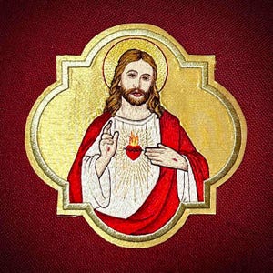 May include: Embroidered patch featuring a depiction of Jesus Christ with a golden halo and a red heart. The figure is dressed in a red robe and white garment, set against a gold and burgundy background. The patch is likely for religious apparel or crafts.