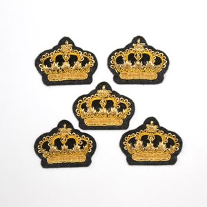 May include: Five gold embroidered crown patches on black felt. The crowns are detailed with intricate designs and are perfect for adding a touch of royalty to any project.