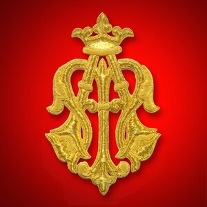 May include: A gold-colored embroidered emblem with a crown and ornate intertwined letters on a red background. The emblem features intricate detailing and a symmetrical design, suggesting a heraldic or decorative element.