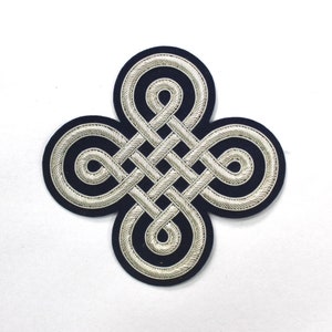 May include: A silver embroidered knot design on a dark blue fabric background. The knot is a traditional symbol of good luck and prosperity.