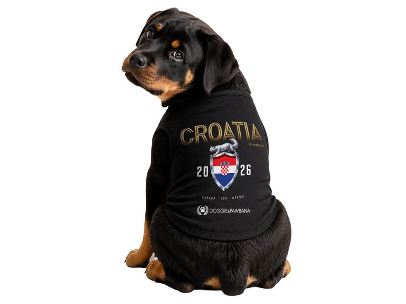 May include: A Rottweiler dog wearing a black shirt with "CROATIA" in gold lettering. The shirt features a shield with the Croatian flag and the year "2026". The shirt also has the text "DOGGIEPAWBANA" and the locations "CANADA USA MEXICO".