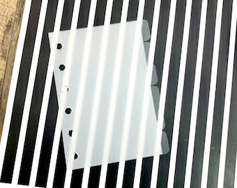 May include: A white plastic sheet with six tabs and a row of six holes down the left side. The sheet is placed on top of a black and white striped background.