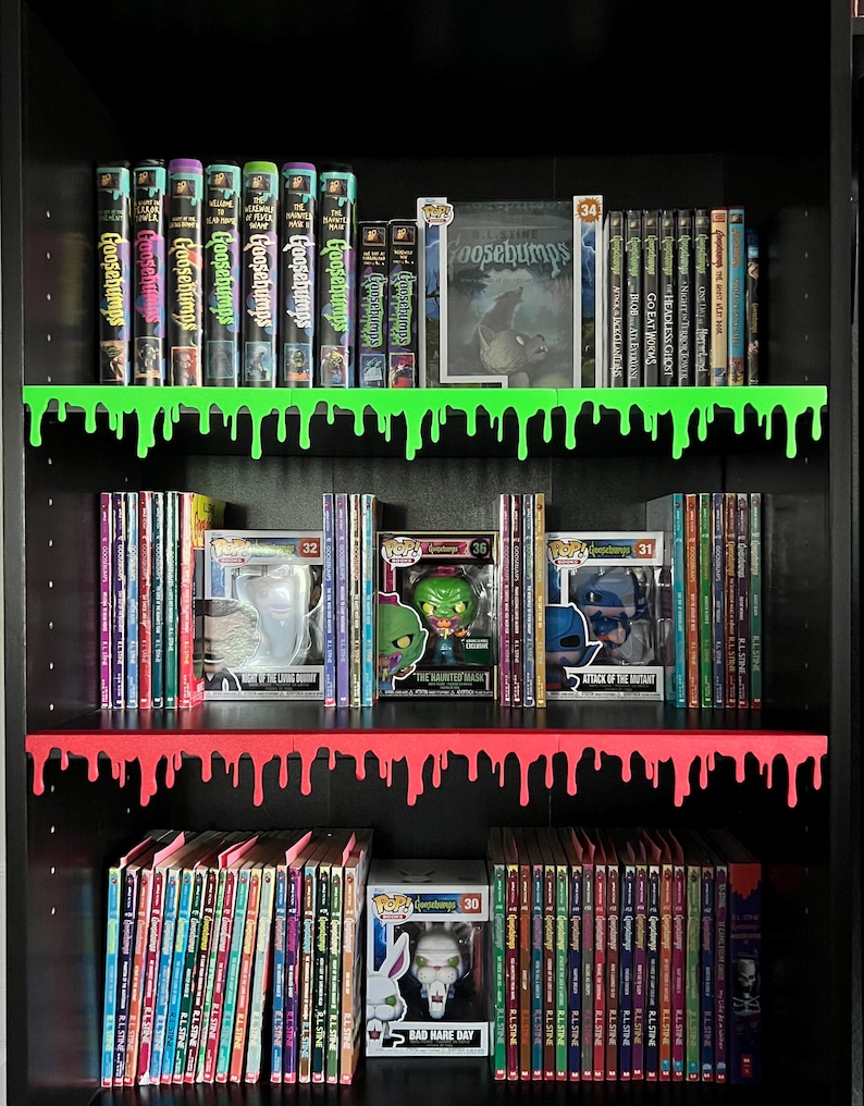 May include: A black bookshelf with green and red dripping shelves, displaying a collection of Goosebumps books, VHS tapes, and DVDs. Funko Pop figures are also visible, including a Bad Hare Day figure.