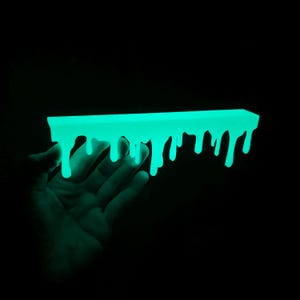 May include: A neon green, rectangular object with a dripping design, set against a black backdrop. The object glows brightly, with the dripping effect creating a unique, artistic appearance. The overall theme is a modern, abstract design, with a striking visual impact.
