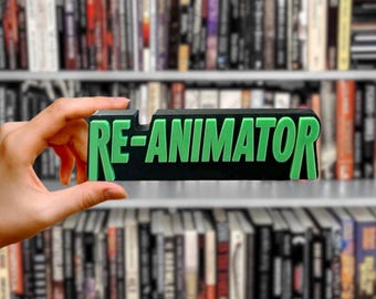 Może przedstawiać: Czarno-zielony znak 3D z napisem "RE-ANIMATOR".