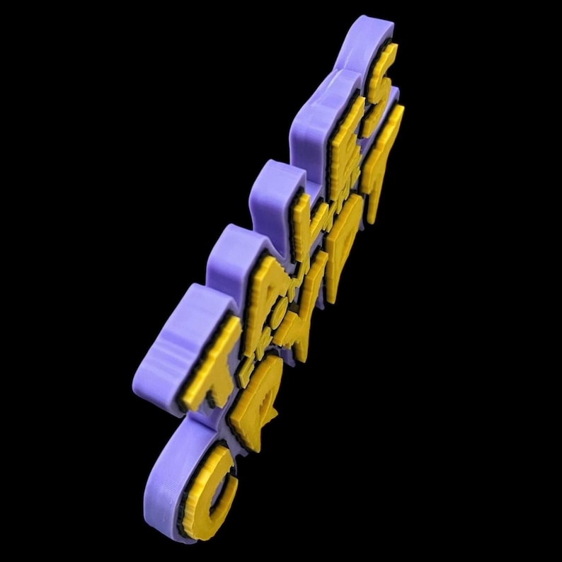 Puede incluir: Una palabra impresa en 3D de color morado y amarillo que dice "GRAPE" con las letras apiladas una encima de la otra.