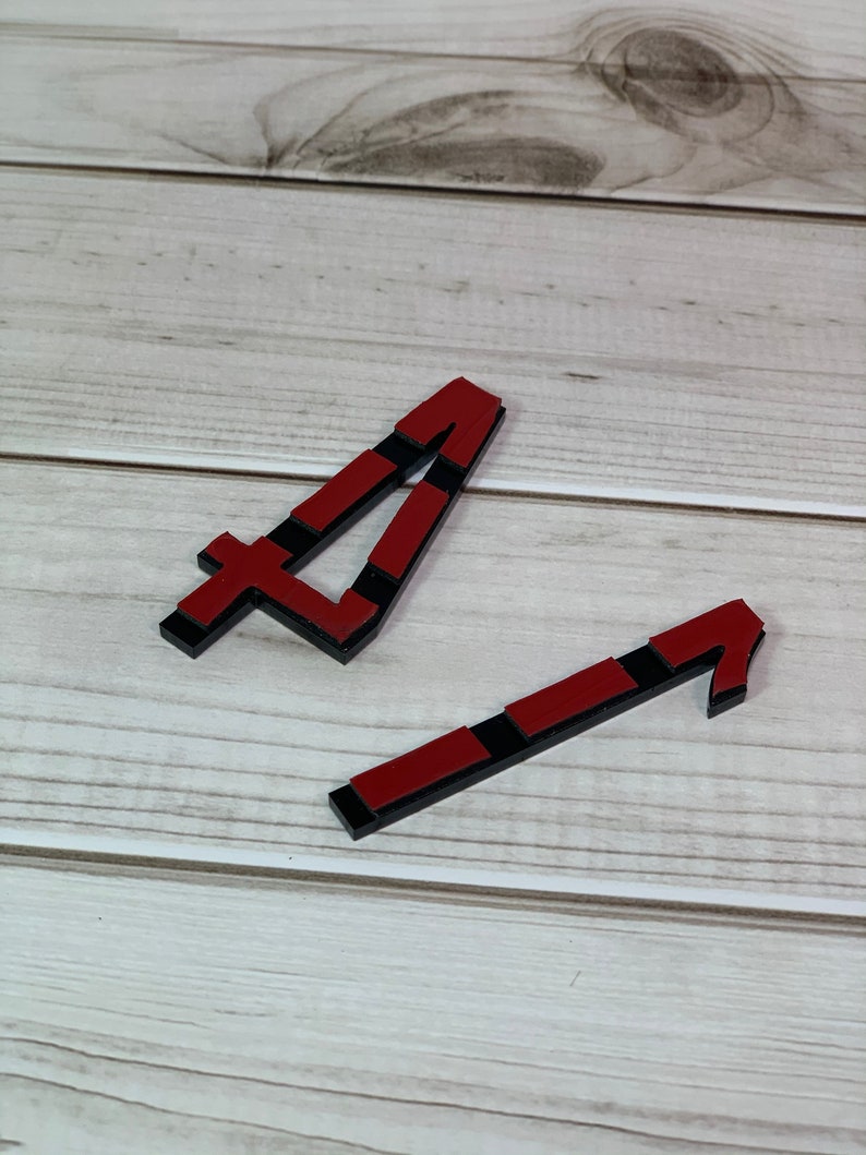 May include: Two wooden number four shapes. The shapes are red with black accents. The shapes are on a light wood grain surface.